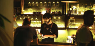 A barman makes cocktails in a green-lit bar, one of puerta vallarta bars best spots.